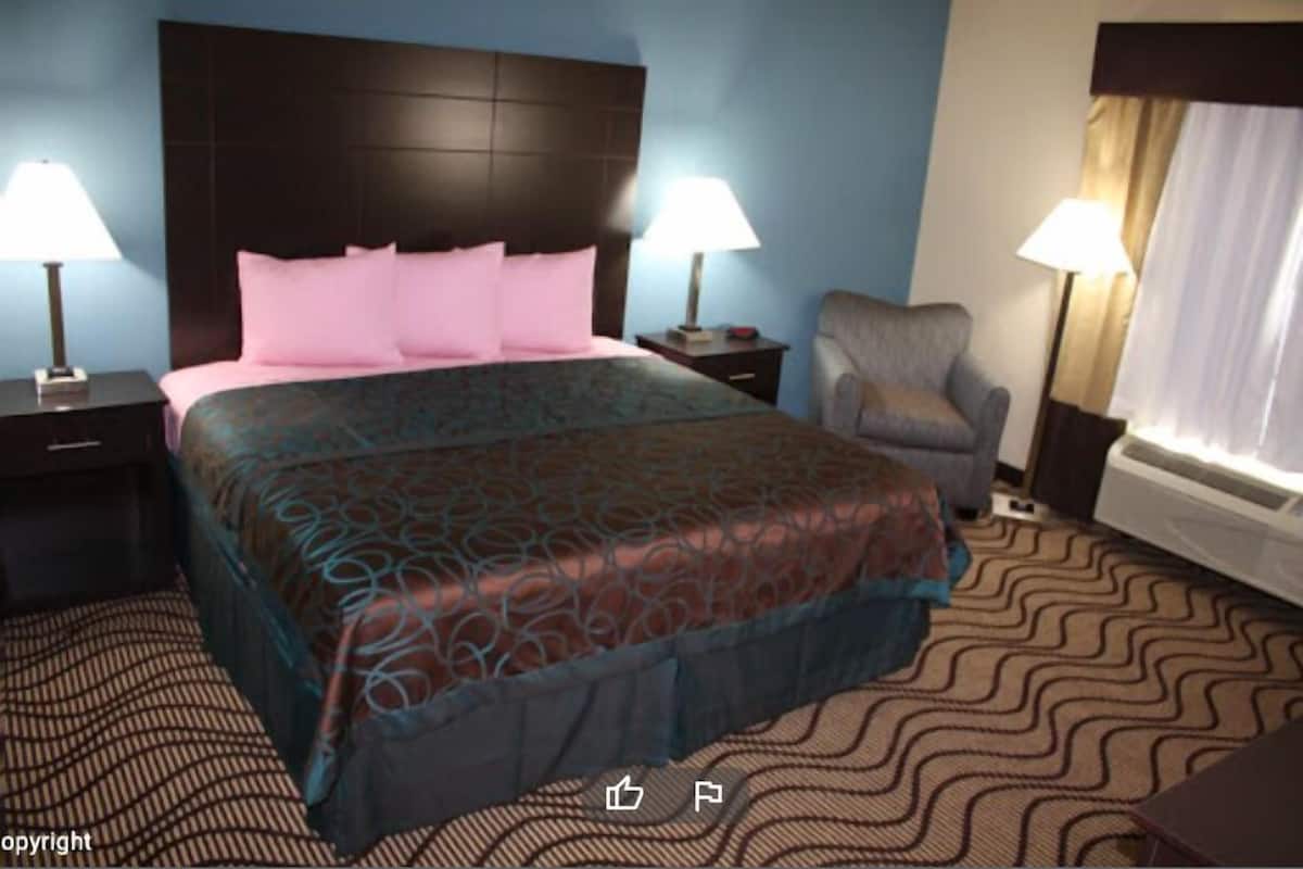 A hotel room with a large bed, two bedside tables with lamps, a chair, and a window with curtains.