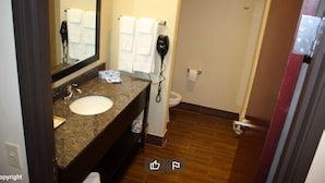 A bathroom with a granite countertop sink, a mirror, a hairdryer, and a toilet. - La Plaza Inn & Suites (Freer)