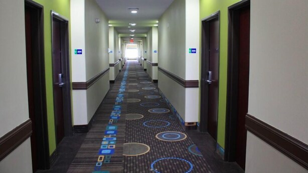 A hotel hallway with carpeted floors, doors on both sides, and a light-colored wall. - La Plaza Inn & Suites (Freer)