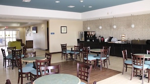 A hotel lobby with round tables and chairs, a reception desk, and a patterned wall. - La Plaza Inn & Suites (Freer)