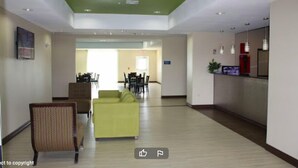 A spacious lobby with a green ceiling, a yellow sofa, and a dining area in the background. - La Plaza Inn & Suites (Freer)