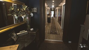Um saguão de hotel com mesa de recepção, espelho, placa de boas-vindas e corredor que dá para outros quartos.