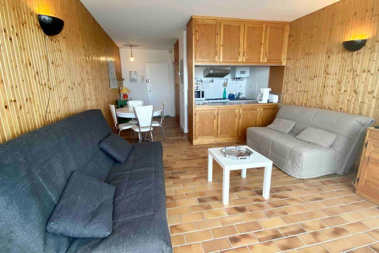 A compact living space with a grey sofa, a light grey sofa, a small white table, and wooden cabinets.