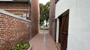 Un estrecho callejón con paredes de ladrillo, una rejilla de metal y una puerta de madera.