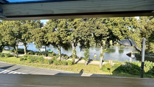 Vista desde el interior de un edificio, sobre un lago con árboles y un sendero.