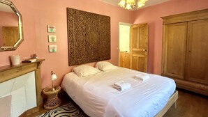 Un dormitorio con cama, espejo, panel decorativo en la pared, armario de madera y una lámpara de noche pequeña.