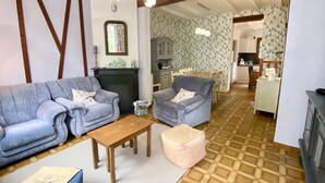 Una sala de estar con sofá, sillón, mesa de madera y reposapiés. Se aprecia una chimenea al fondo.