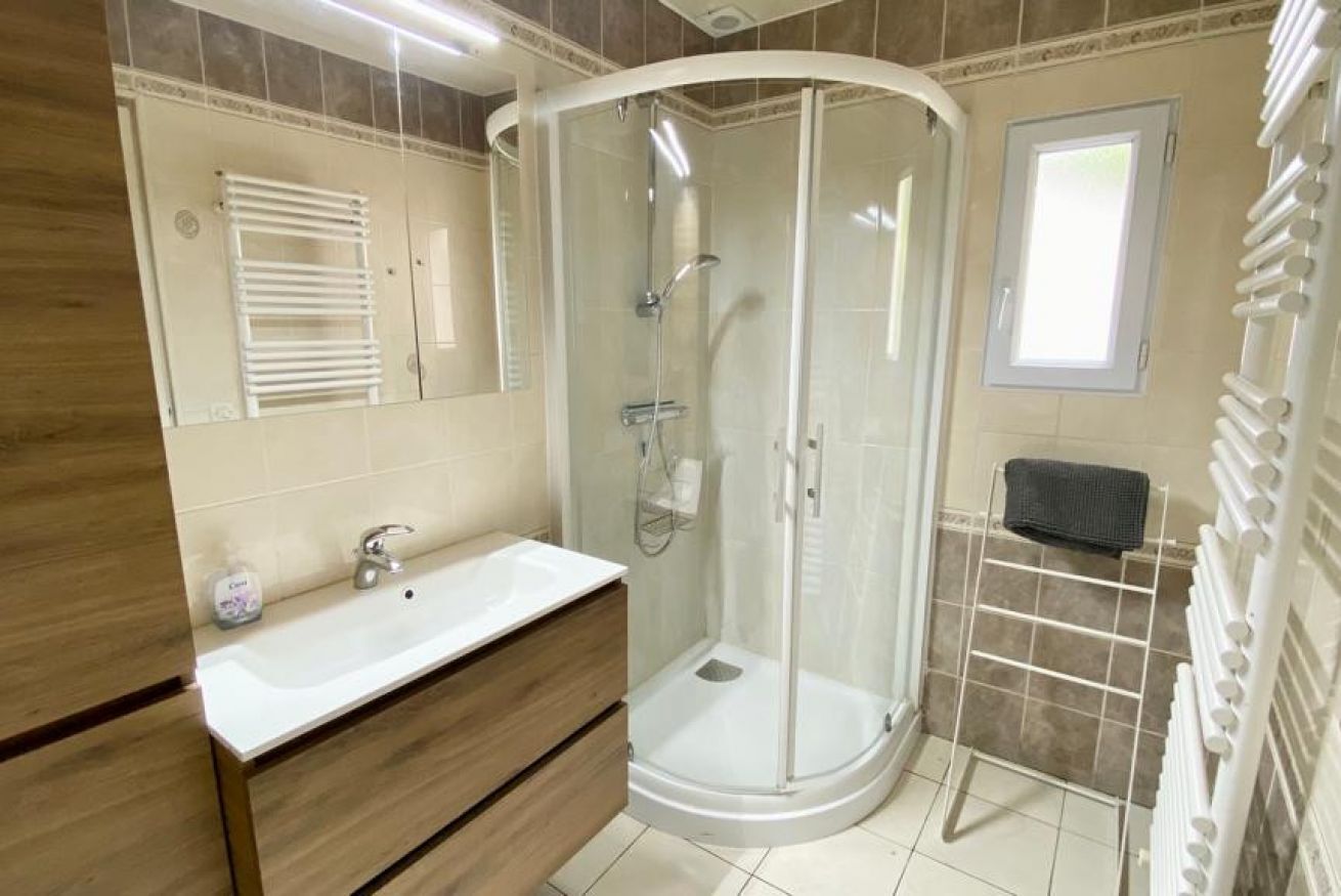 A bathroom with a white sink, wooden vanity, a glass shower enclosure, and a towel rack.