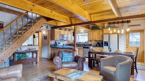 A spacious living area with a wooden staircase, a dining table set for four, and a kitchen with modern appliances.