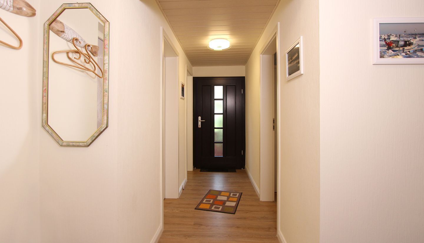Ein Korridor mit Holzboden, einer Tür am Ende und einem gerahmten Bild an der Wand.