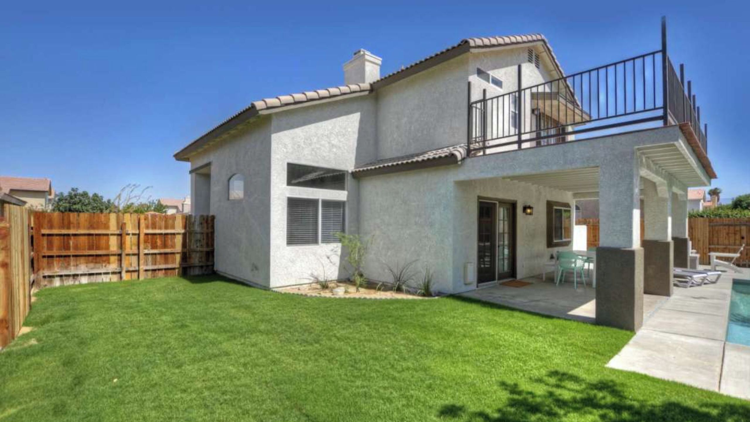 A two-story house with a covered patio, a swimming pool, and a fenced backyard.
