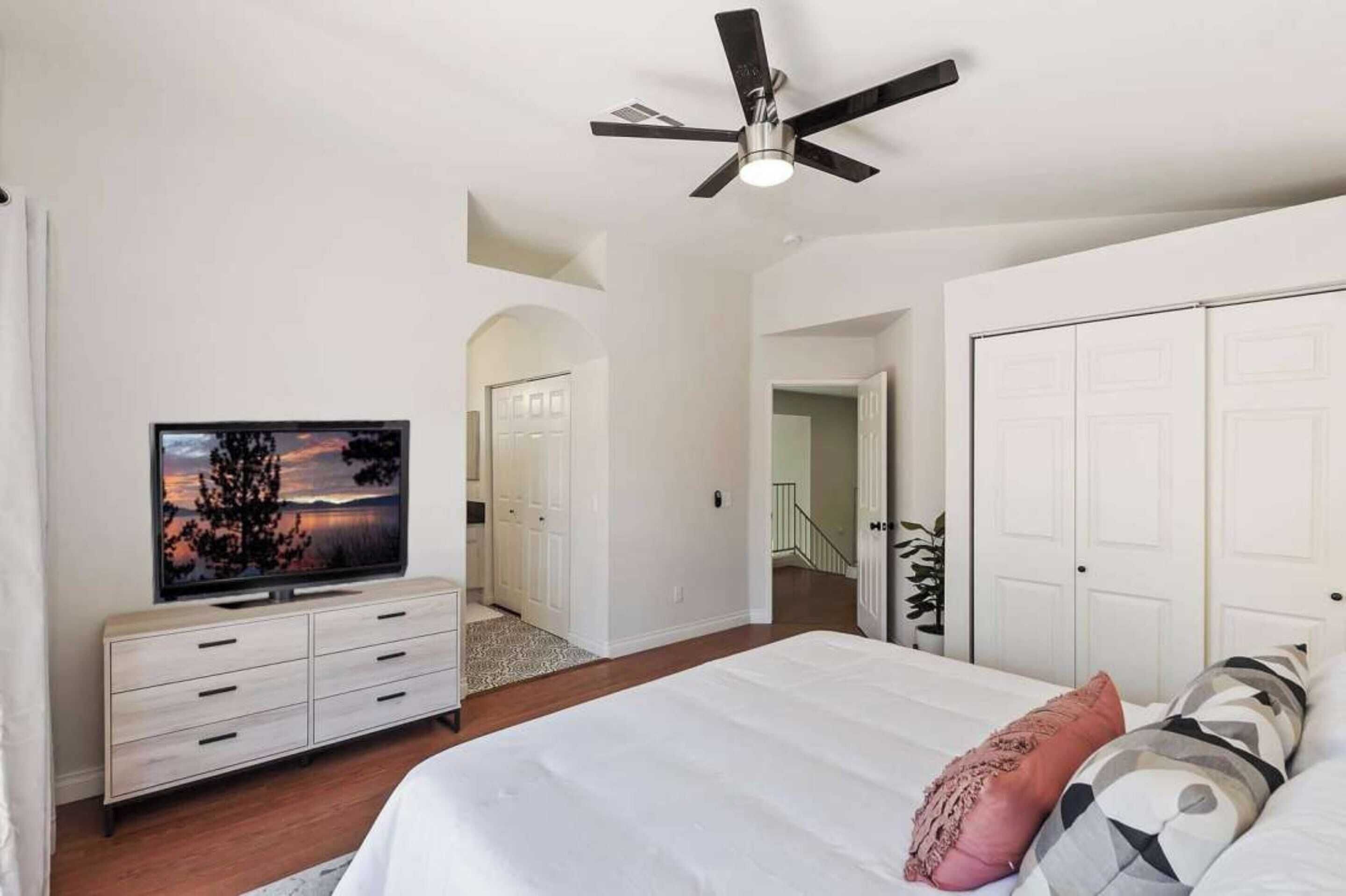 Un dormitorio con cama, televisor, ventilador de techo y armario.