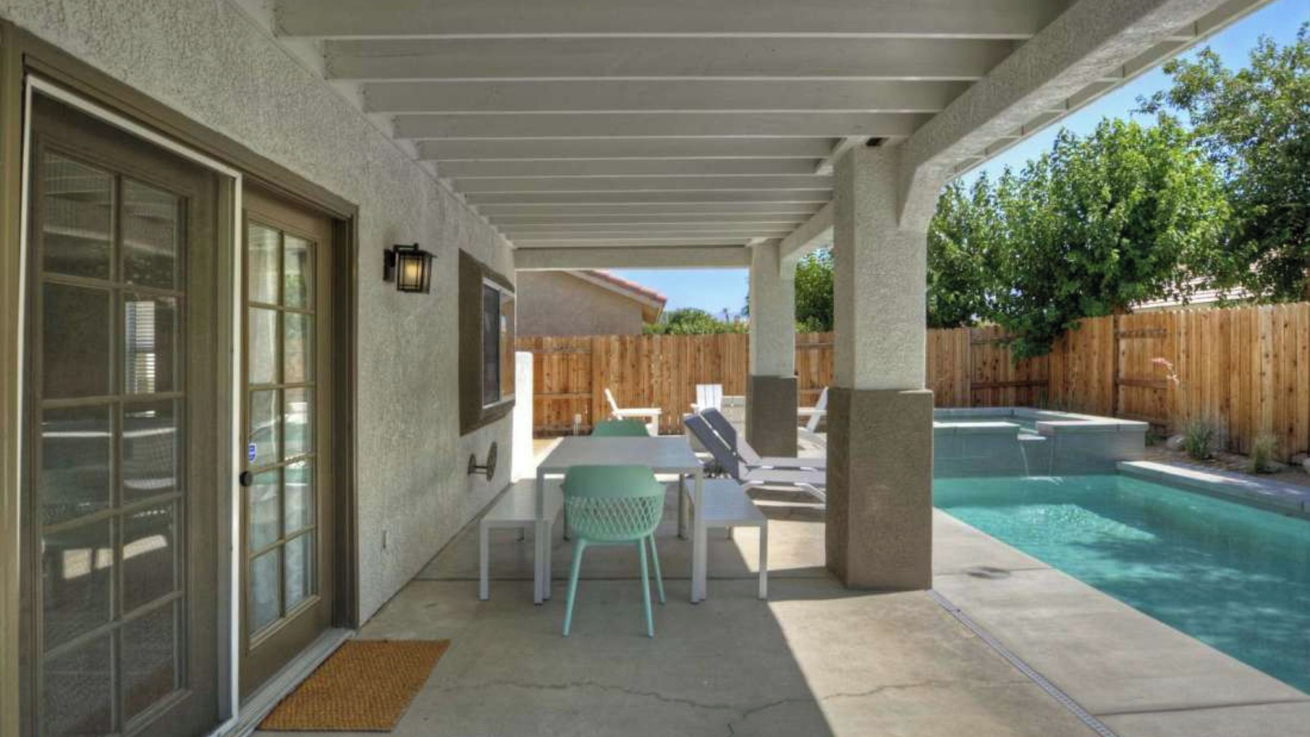 Une terrasse couverte avec une piscine, des sièges d’extérieur et une clôture en bois.