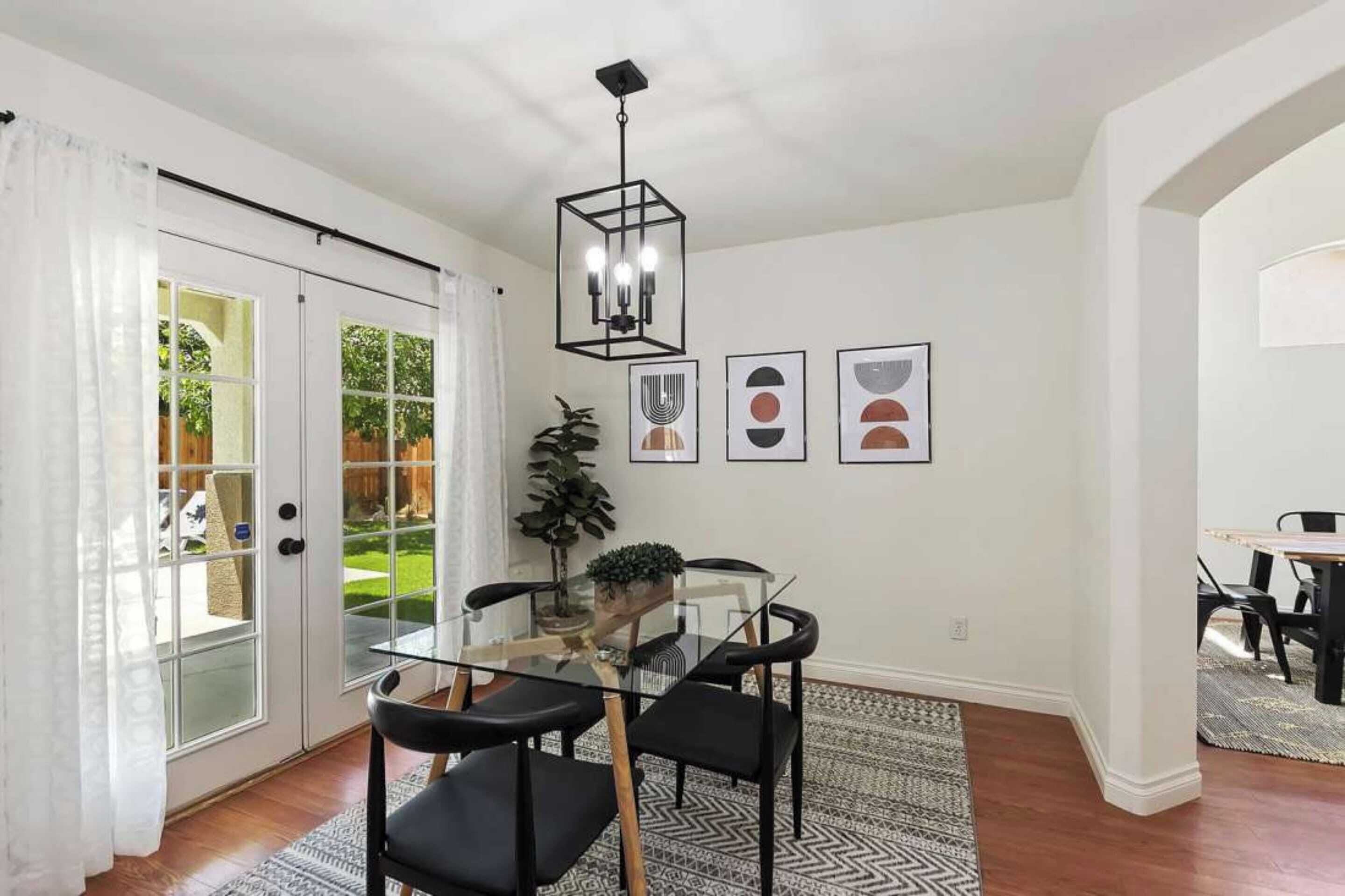 Un coin repas avec une table en verre et des chaises noires, un luminaire suspendu et des œuvres d’art encadrées accrochées au mur.