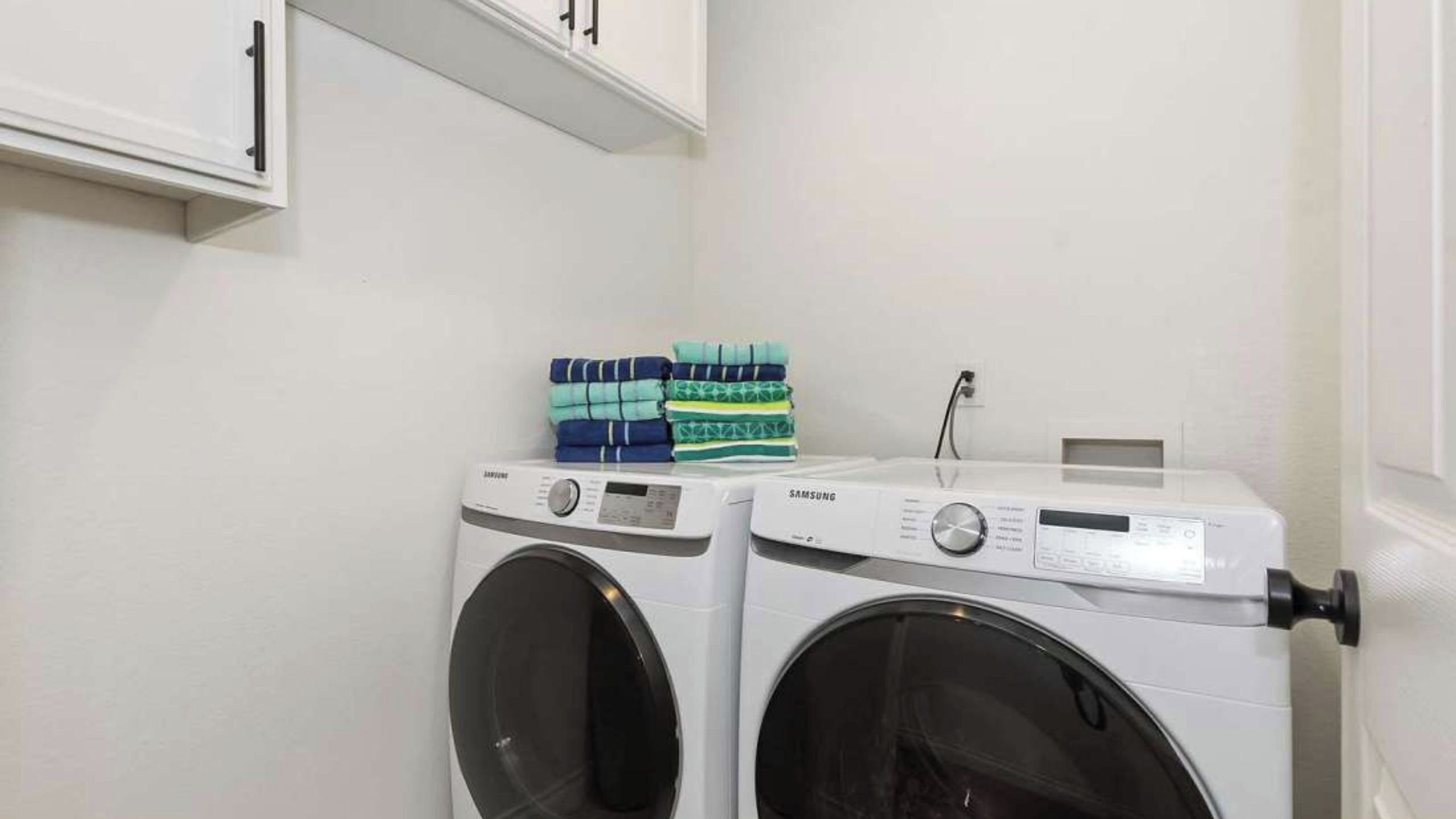 A laundry area with two washing machines, a shelf with folded towels, and a wall-mounted cabinet.