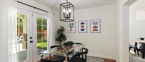 A dining area with a glass table, black chairs, a hanging light fixture, and framed artwork on the wall.