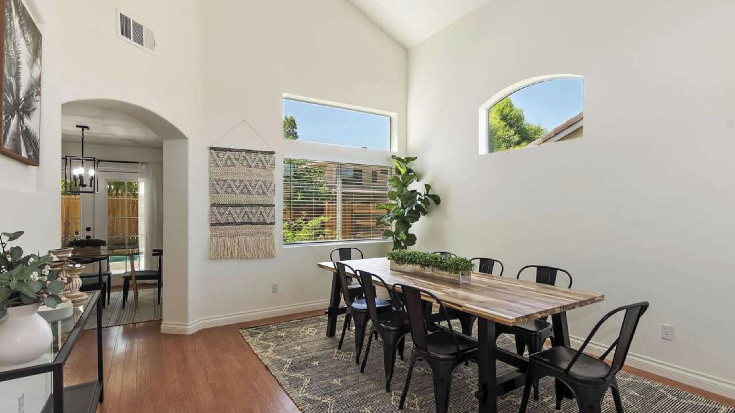 Un coin repas avec une table en bois, des chaises noires, une décoration murale à motifs et une grande fenêtre donnant sur un paysage verdoyant.