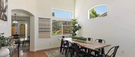 Un coin repas avec une table en bois, des chaises noires, une décoration murale à motifs et une grande fenêtre donnant sur un paysage verdoyant.