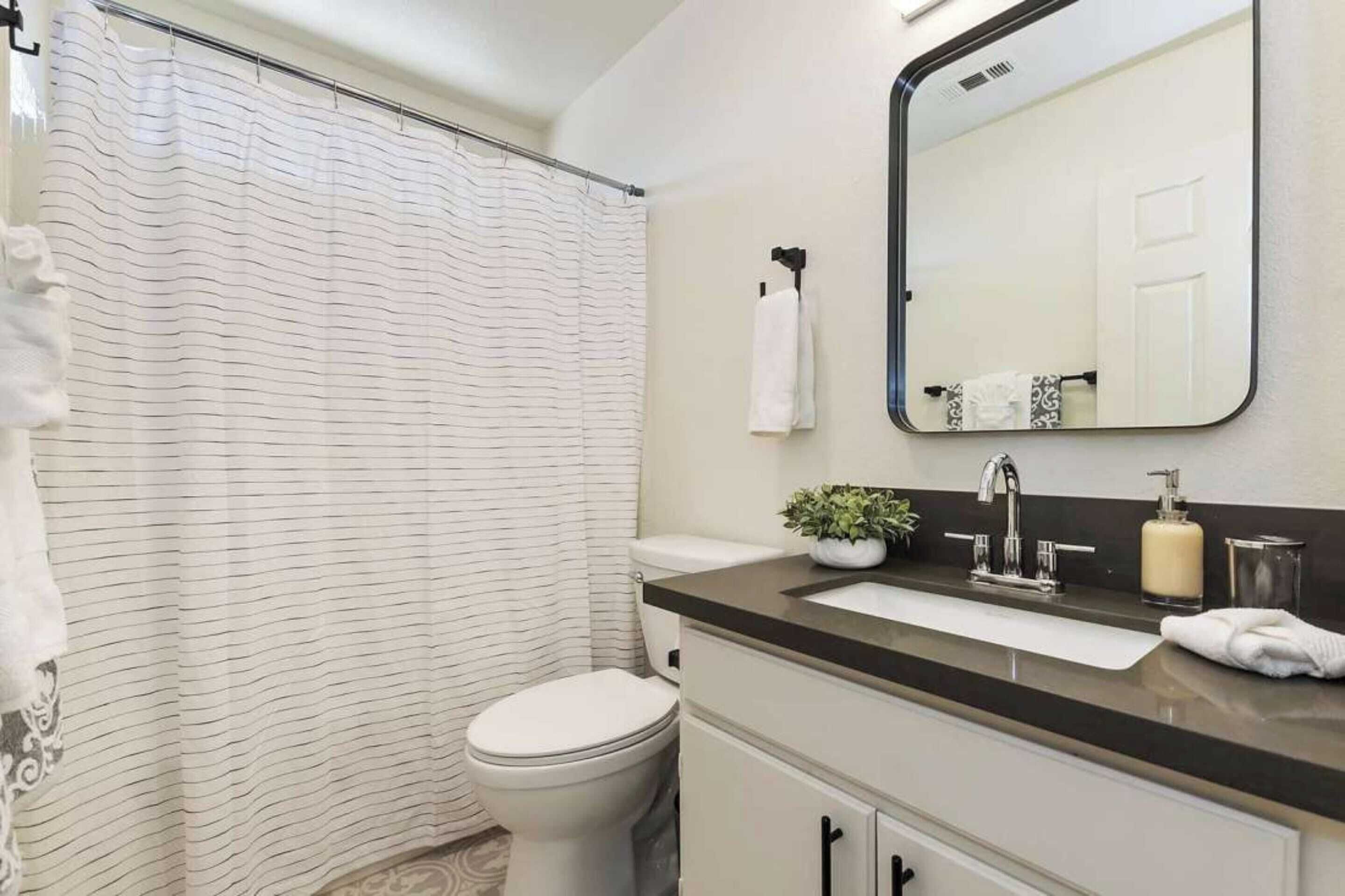 A bathroom with a shower curtain, toilet, sink with a mirror, and a towel rack.