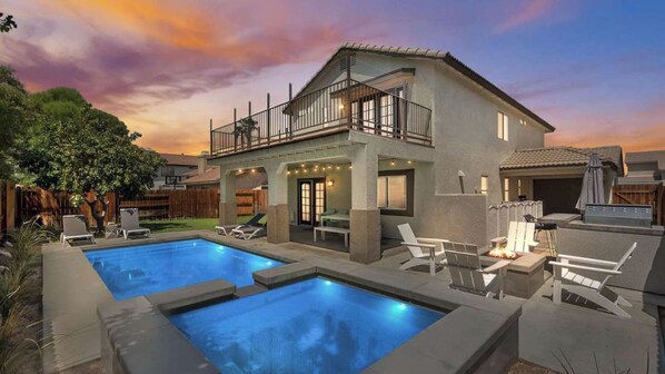 Une maison à deux étages avec une piscine, un espace salon extérieur et une terrasse couverte.
