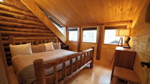 A wooden cabin bedroom with a bed, a desk, and a window.