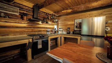 A rustic kitchen with wooden walls, a gas stove, a stainless steel refrigerator, and a wooden dining table.