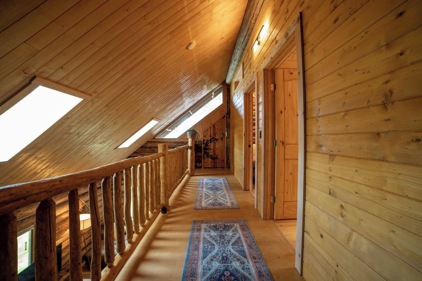 A wooden interior with a sloped ceiling, a wooden railing, and a patterned rug.