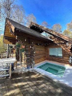 A log cabin with a wooden deck, a small outdoor pool, and a covered patio area.