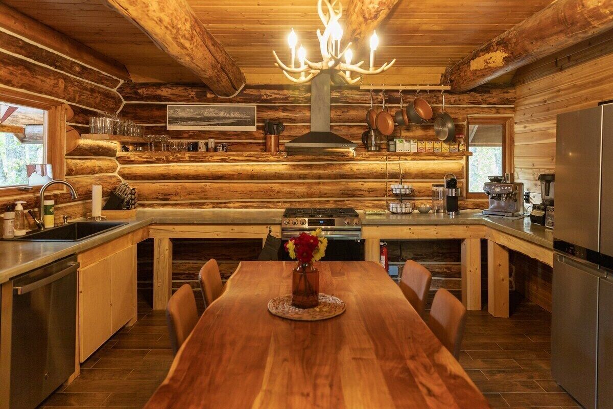 A log cabin kitchen with a wooden dining table, a chandelier, and a stove.