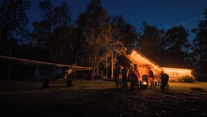 A rustic cabin with a dining area and a parked airplane.
