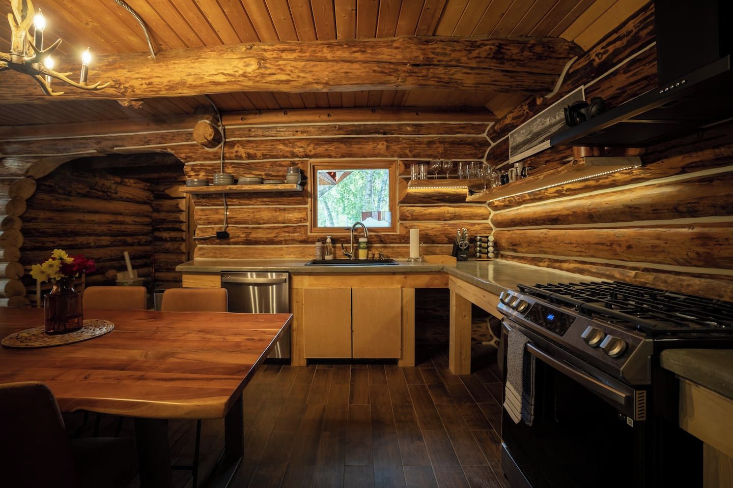 A log cabin interior with a wooden dining table, a kitchen with a stove, and a map on the wall.