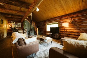 Een blokhut interieur met een open haard, houten wanden, een bank en een televisie.