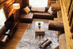 Interior acogedor de una cabaña de troncos con sofá, reposapiés y una mesita de centro.