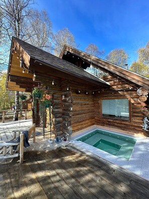 Una cabaña de troncos con terraza de madera, una piscina pequeña y un banco.