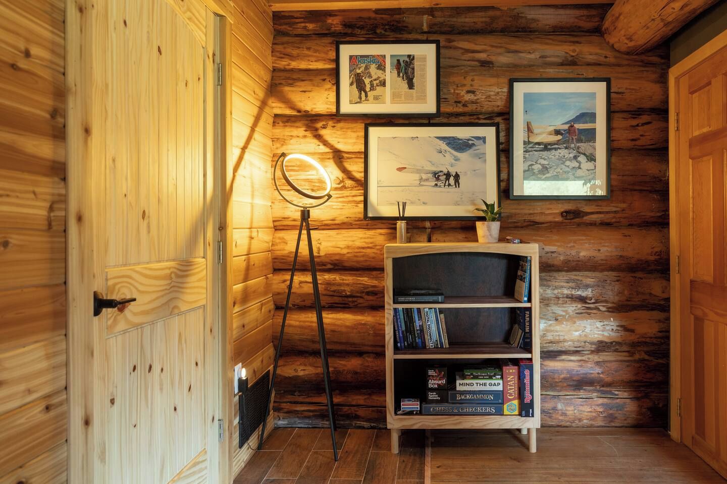 A wooden interior with a bookshelf, framed pictures, and a floor lamp.