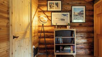A wooden interior with a bookshelf, framed pictures, and a floor lamp.