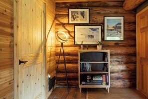 A wooden interior with a bookshelf, framed pictures, and a floor lamp.