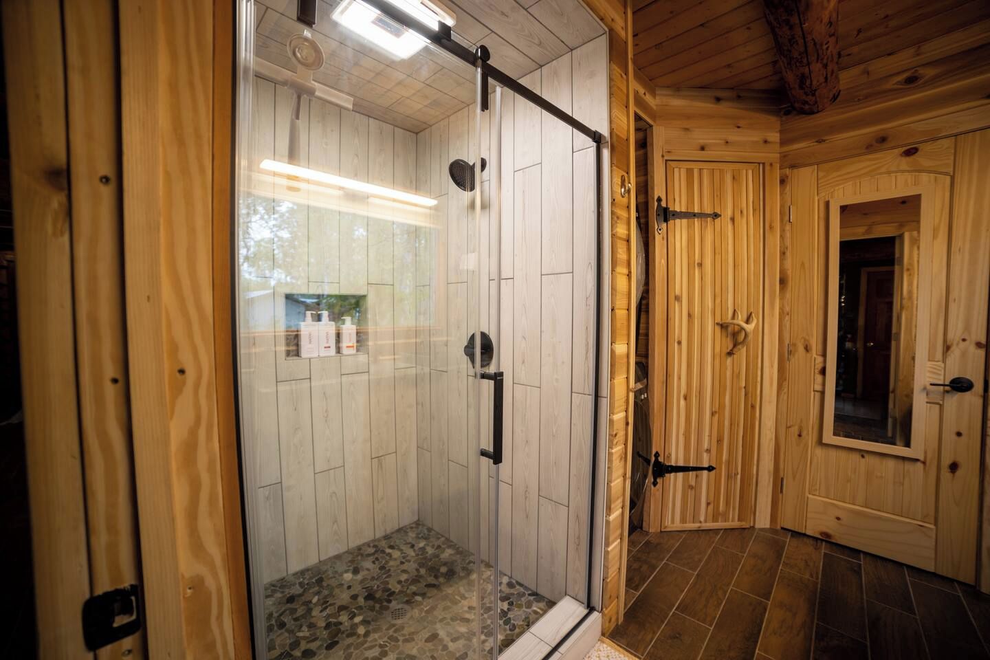 A wooden cabin with a glass-enclosed shower area and a door leading to another room.