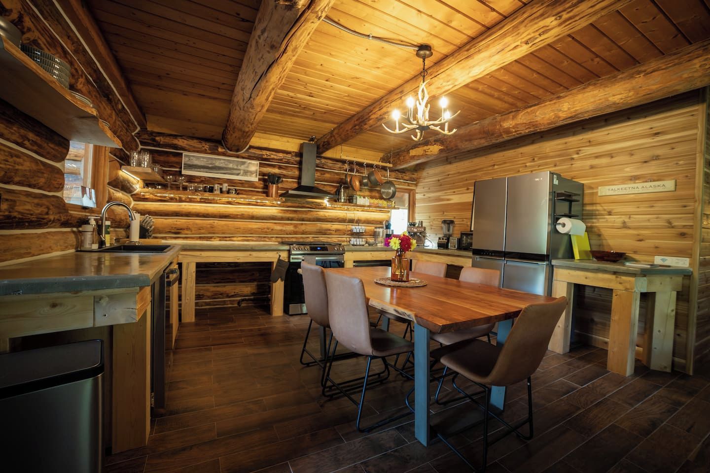 Ein rustikales Blockhaus-Interieur mit einem Holzespeise-Tisch, Stühlen, einer Küchenzeile mit Herd und Kühlschrank.