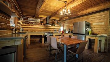 Ein rustikales Blockhaus-Interieur mit einem Holzespeise-Tisch, Stühlen, einer Küchenzeile mit Herd und Kühlschrank.