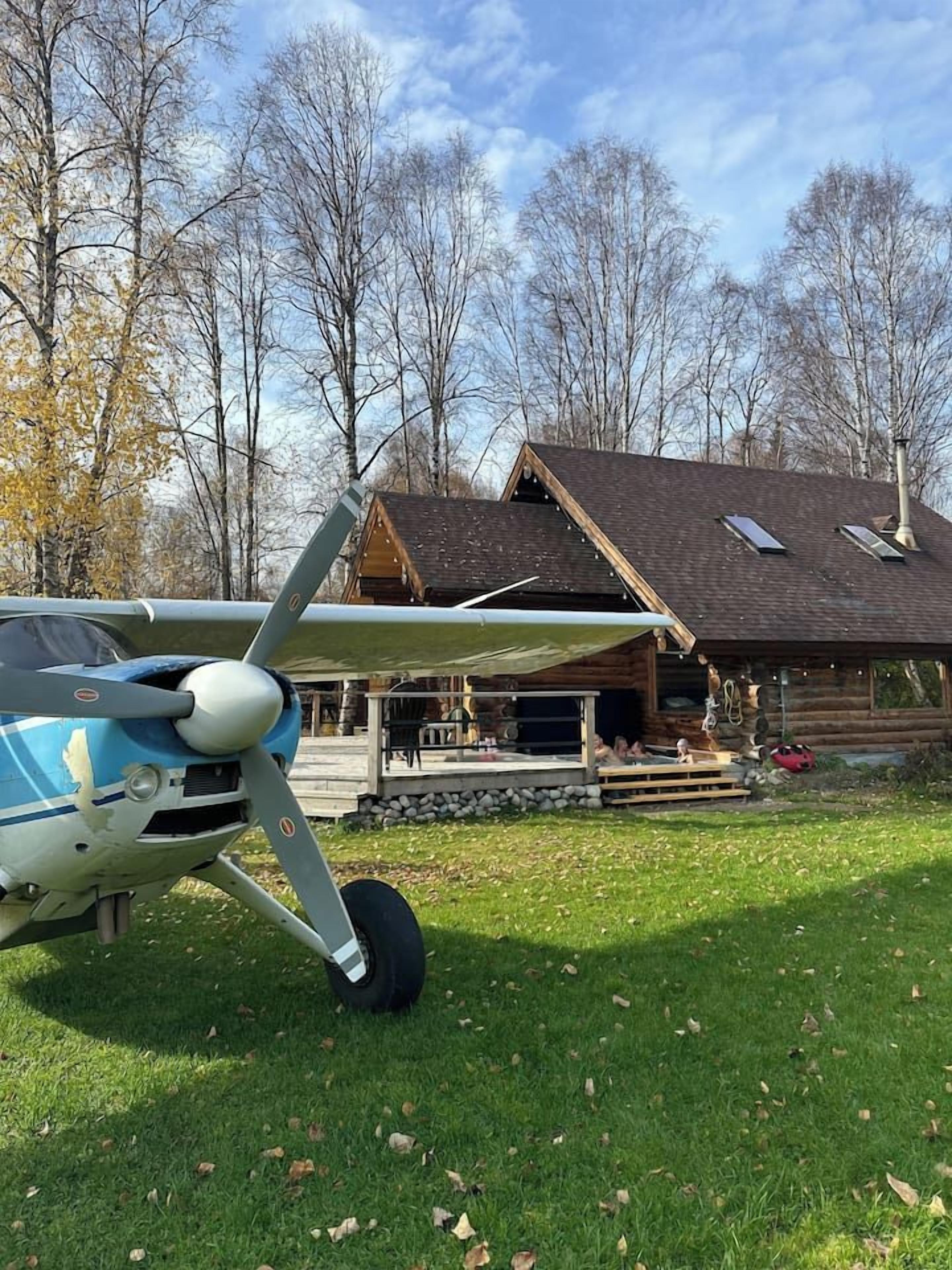A small airplane parked in front of a wooden cabin with a covered outdoor area.