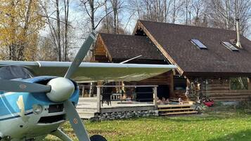 A small airplane parked in front of a wooden cabin with a covered outdoor area.