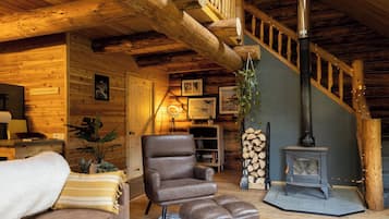 A cozy cabin interior with a wooden staircase, a leather armchair, a fireplace, and a sign reading 'Talkeetna Alaska'.