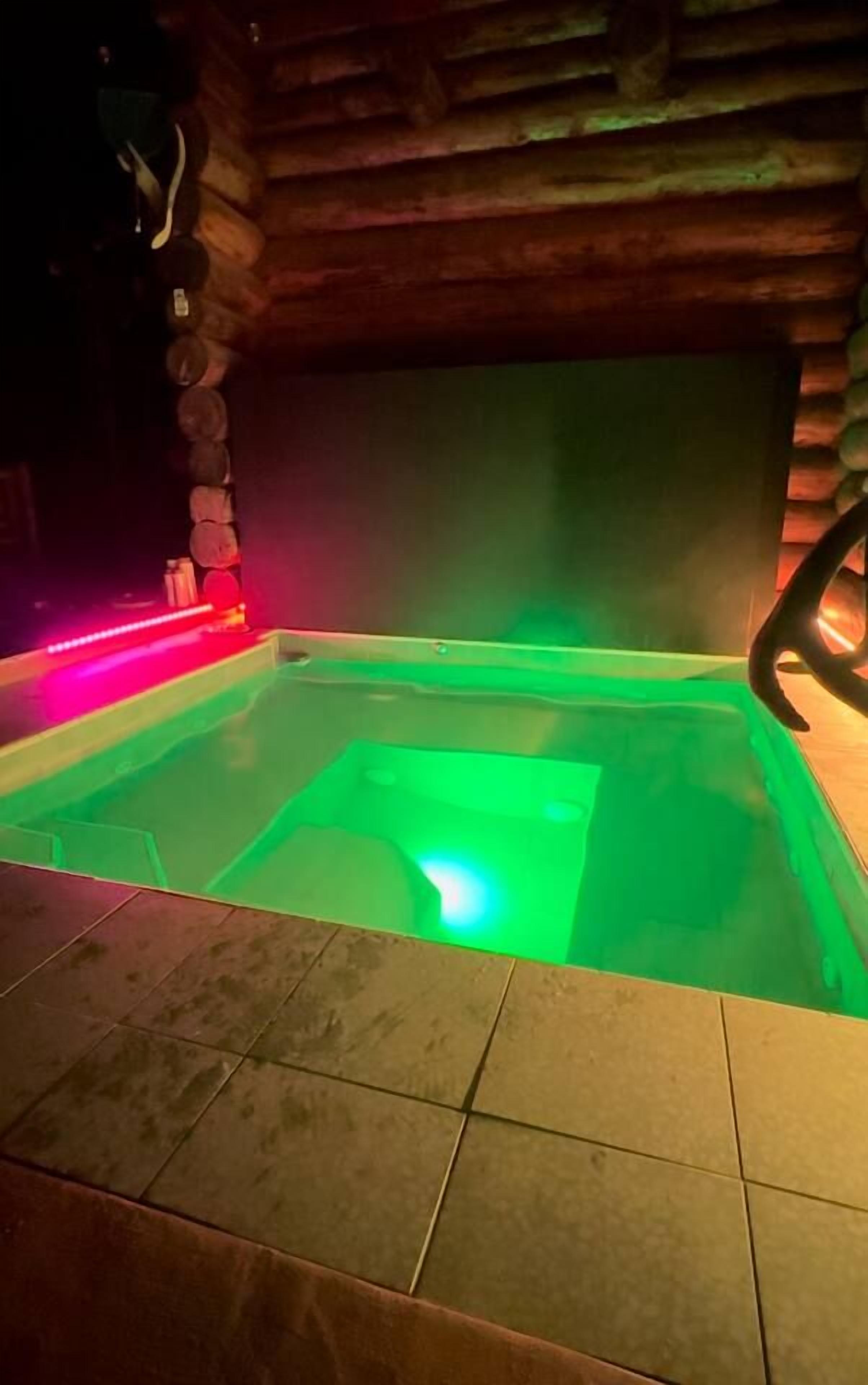 A hot tub with green lighting, surrounded by tiled flooring, and wooden walls.