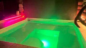 A hot tub with green lighting, surrounded by tiled flooring, and wooden walls.