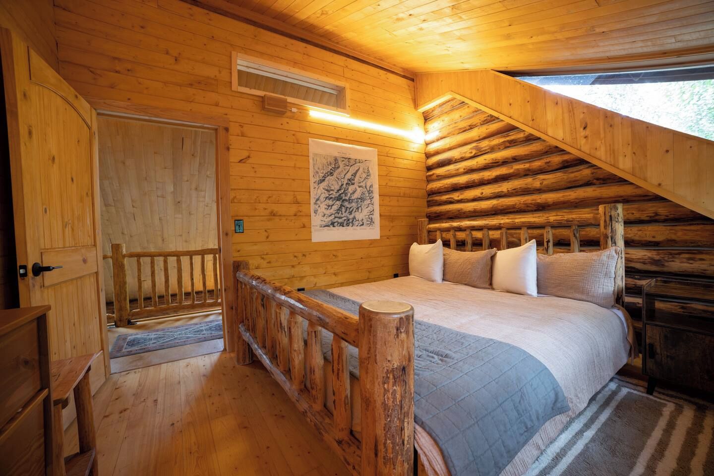 Een slaapkamer in een blokhut met een bed, houten wanden, een raam en een deur.