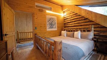 Een slaapkamer in een blokhut met een bed, houten wanden, een raam en een deur.