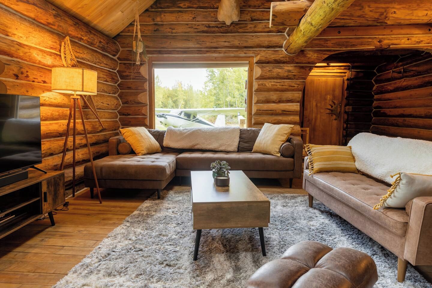 A log cabin interior with a sectional sofa, a television, and a coffee table.