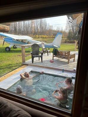 Een bubbelbad met mensen die ontspannen, een klein vliegtuig en tuinmeubilair in een achtertuin.