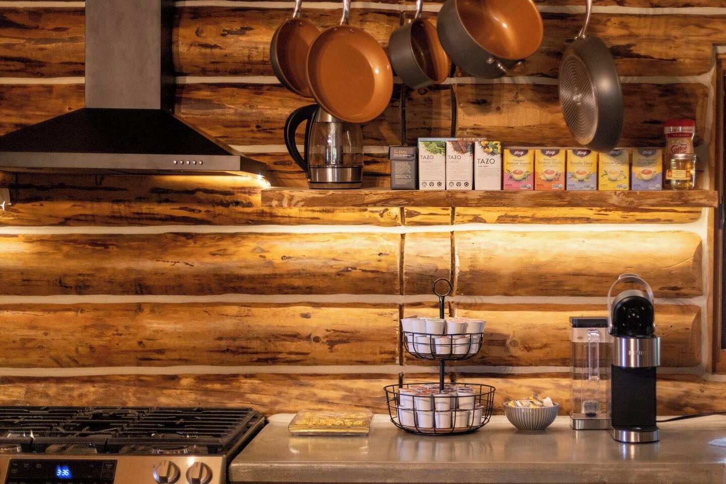 A kitchen with a wooden wall, hanging pots, a coffee machine, and a stove.